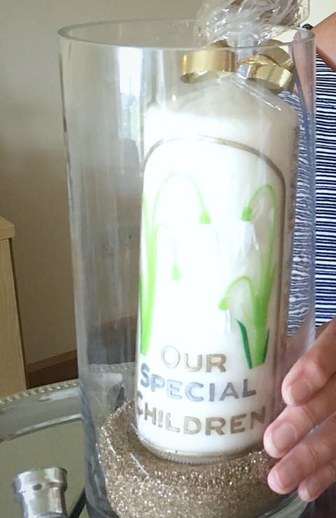 Candle decorated with snowdrops and the words Our Special Children, in a glass vase